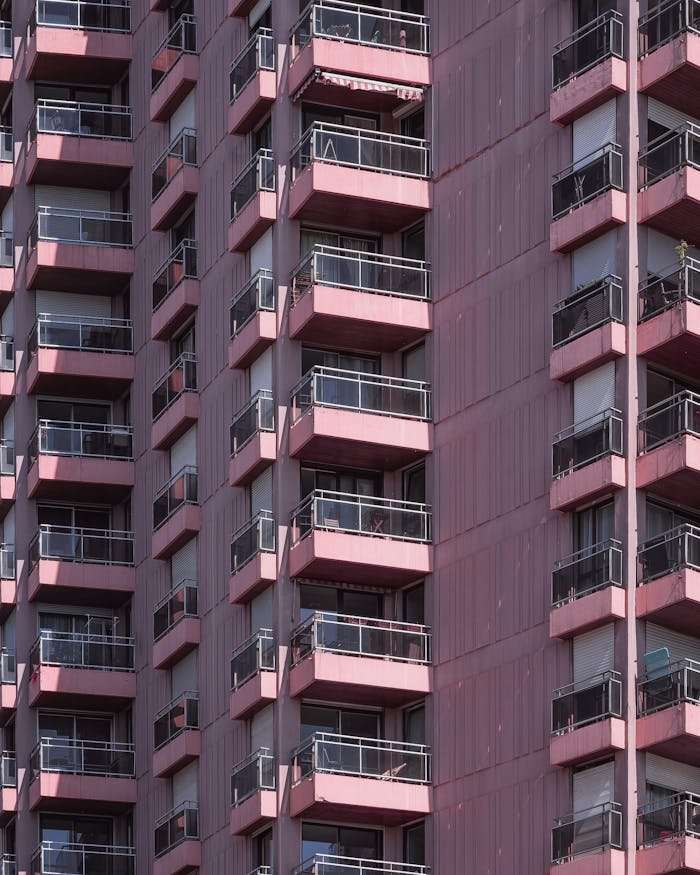 Modern pink apartment building facade with repeating balconies and glass windows.