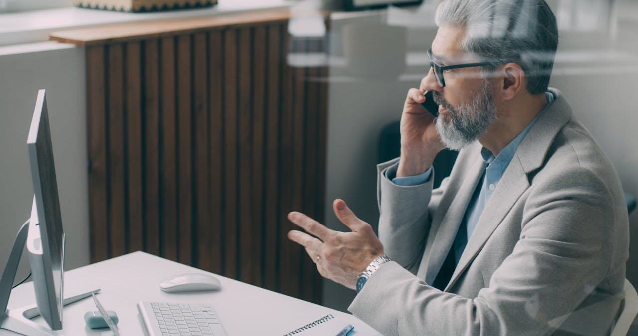 Senior businessman speaking on phone at desk in a modern office setting, emphasizing connectivity and professionalism.